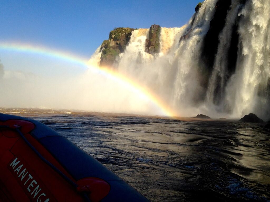 Barco do Macuco Safari diante das quedas do rio Iguaçu, com arco-íris